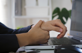 Personne tenant son poignet avec l'autre main, travaillant sur un ordinateur portable, suggérant une gêne ou une douleur au poignet.